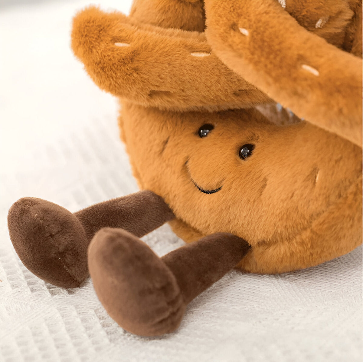 Coussin en peluche en forme de bretzel de 18 cm, posé sur un lit